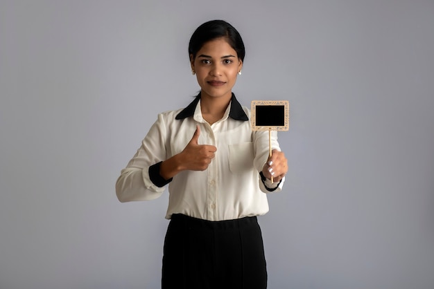 Young woman or business woman holding a little cutout board in her hands on a gray wall.