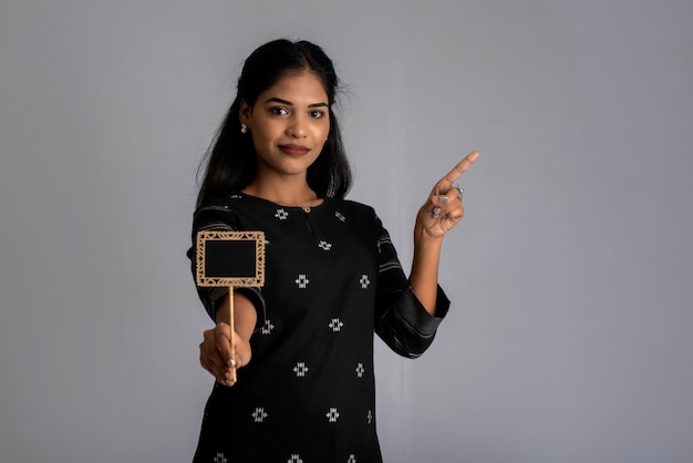 A young woman or businesswoman holding a little cutout board in her hands on a gray wall.