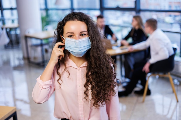 Giovane donna d'affari con una maschera che lavora in ufficio durante la pandemia di coronavirus.