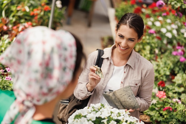 A young woman buying flowers from young woman entrepreneur at a garden center.