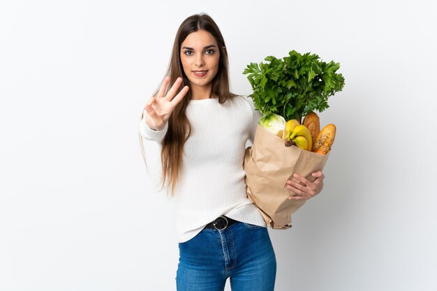 Young woman buying some food isolated on white wall happy and counting three with fingers