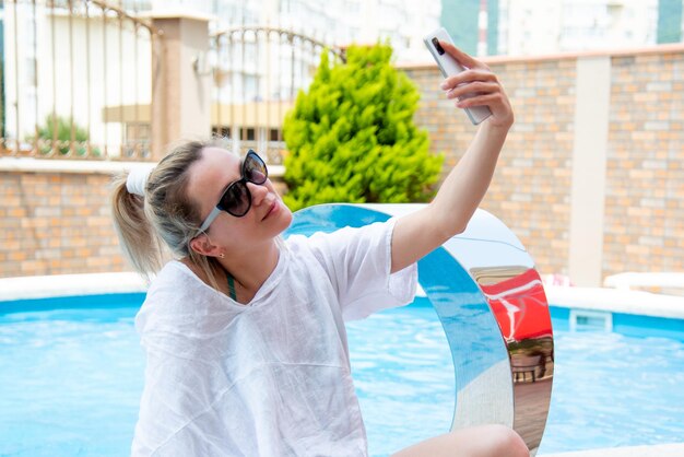 A young woman by the pool with a gadget and coffee in her hands.