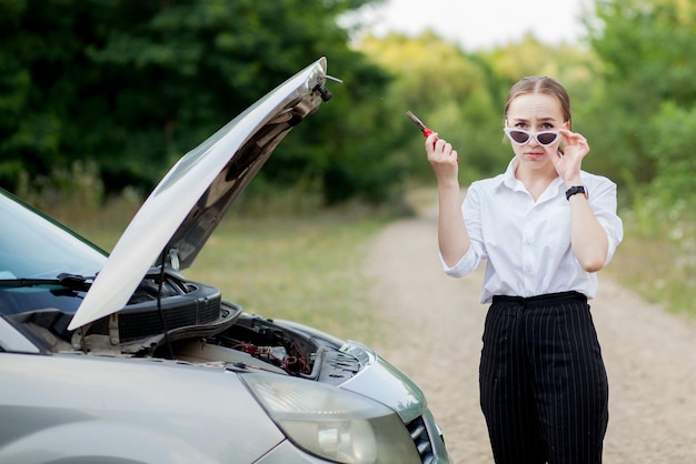 彼女の車が壊れた後、道端で若い女性彼女はフードを開けて損傷を確認しました