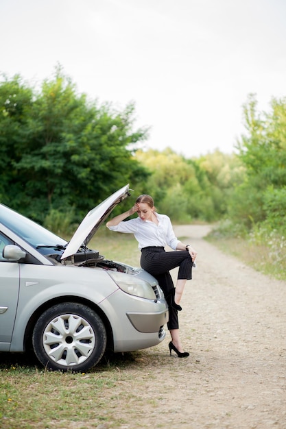 車が故障した後道路沿いの若い女性は損傷を見るためにハードを開けました