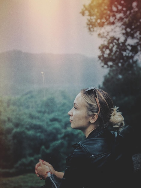 Young woman by tree against sky