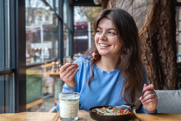 A young woman in a cafe dines on traditional shakshuka and ayran