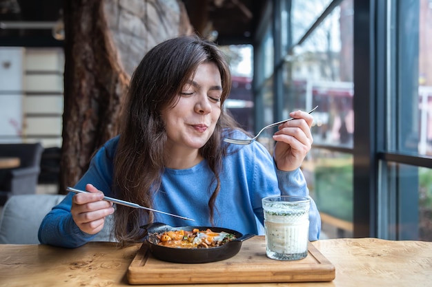 A young woman in a cafe dines on traditional shakshuka and ayran