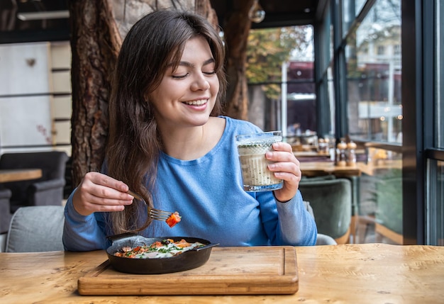 A young woman in a cafe dines on traditional shakshuka and ayran