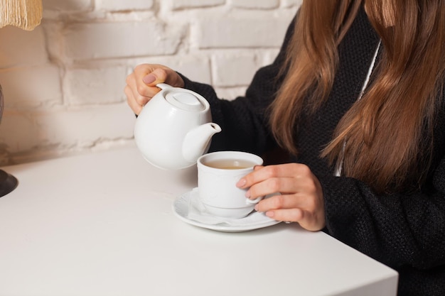 Молодая женщина в кафе пьет здесь любимый напиток чай в белой чашке