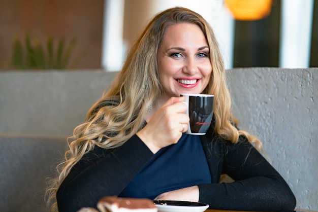 La giovane donna in un caffè beve il caffè in un negozio donna felice che sorride con una tazza di cappuccino