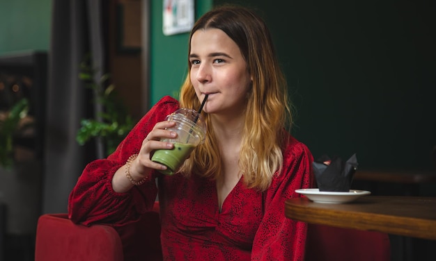 A young woman in a cafe drinks a green drink ice latte