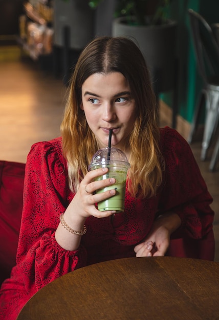 A young woman in a cafe drinks a green drink ice latte