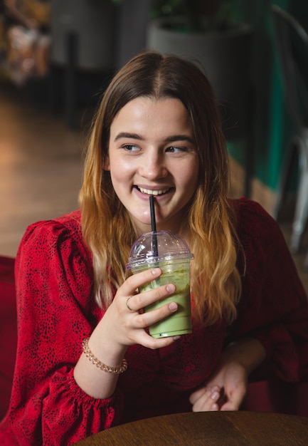 Una giovane donna in un caffè beve una bevanda verde latte ghiacciato