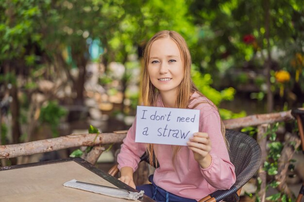 Photo young woman in a cafe shows a sign i dont need a straw no plastic global environmental protection