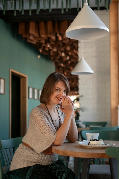 Young woman in cafe with cup of latte or cappuccino and dessert Flirtatious girl sits at table in cafe