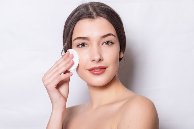 Young woman cares for face skin. Girl removes makeup with cotton ball from face. Young woman cleans skin from cosmetic by cotton swab. Skin care concept.