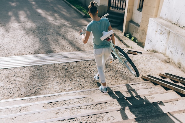 Young woman carries her bicycle on the stairs