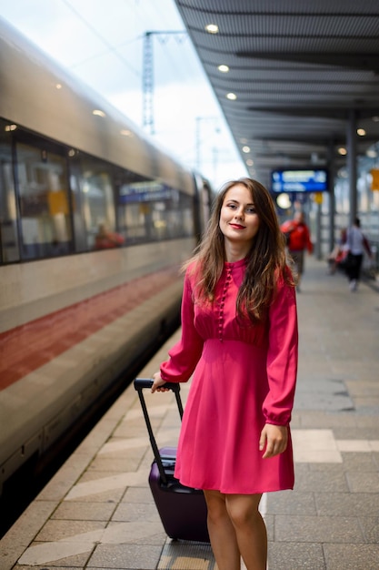 Young woman carrying big suitcase and going to the train at the railway station