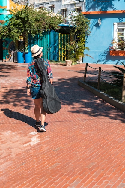 A young woman carrying a guitar while standing in the park