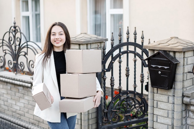 Young woman carrying parcels home standing with a heap of cardboard boxes Concept of buying goods online and delivering them home