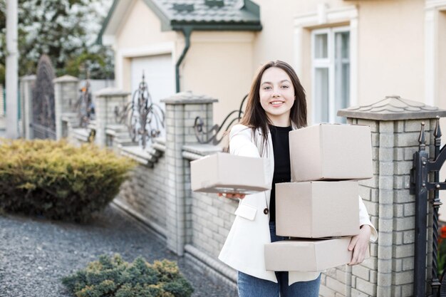 段ボール箱の山で家に立って小包を運ぶ若い女性オンラインで商品を購入し、それらを家に届けるという概念