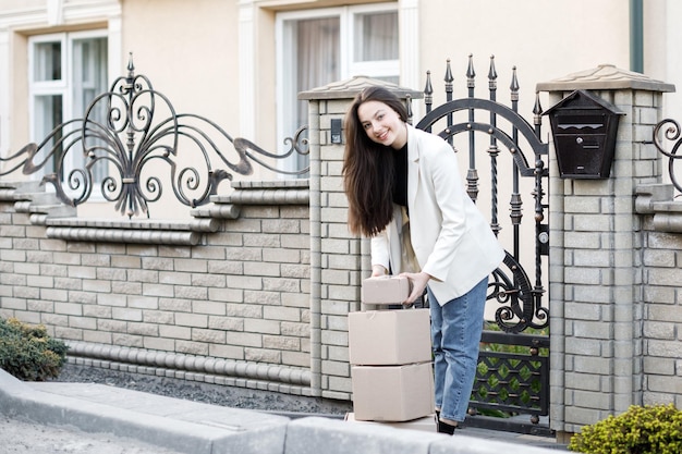 Young woman carrying parcels home standing with a heap of cardboard boxes Concept of buying goods online and delivering them home