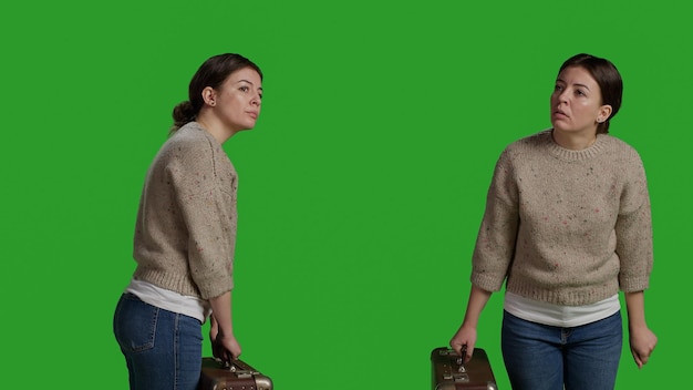 Young woman carrying vintage briefcase in front of camera, holding suitcase in studio before leaving on journey. Cheerful person acting optimistic and having travel bags or luggage over greenscreen.