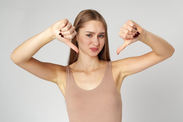 Young woman in casual attire giving thumbs down gesture on gray background