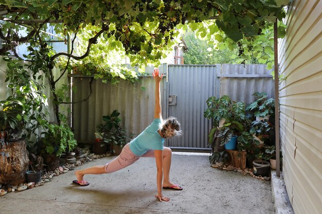 Young woman in casual clothes doing exercises in the courtyard under grapes overhead