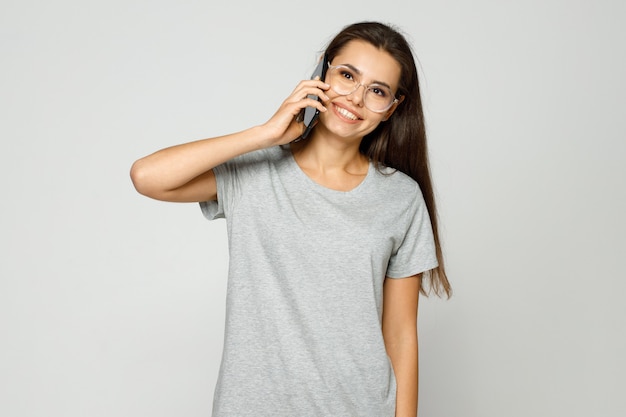 Young woman in casual clothes and glasses talking on smartphone and expresses happiness