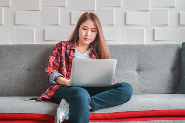 Young woman in casual clothes using laptop computer sitting relaxed working on home sofa couch 