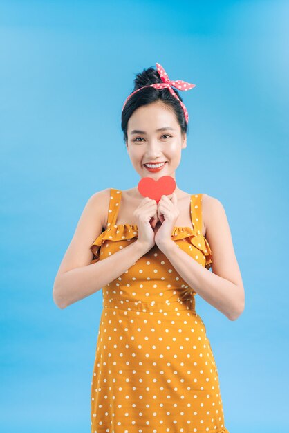 Young woman in casual dress posing with red heart isolated on blue