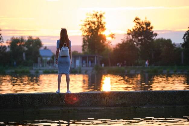 Young woman in casual outfit relaxing on lake side on warm evening. Summer vacations and travelling concept.