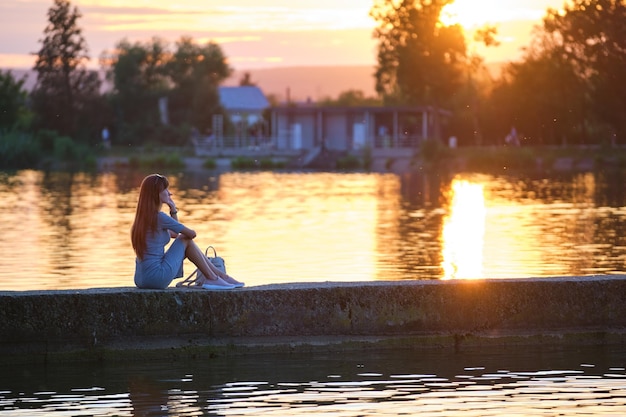 Young woman in casual outfit relaxing on lake side on warm evening Summer vacations and travelling concept