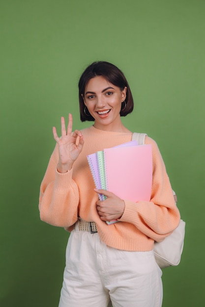 Young woman in casual peach sweater and backpack isolated on green olive color wall