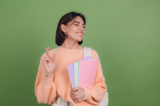 Young woman in casual peach sweater and backpack isolated on green olive color wall