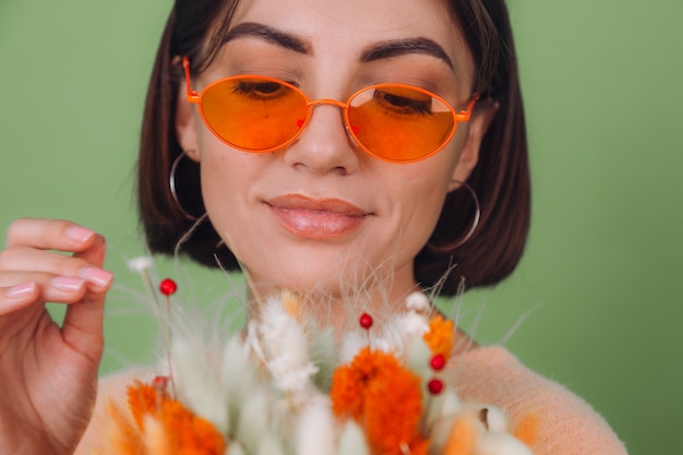 Young woman in casual peach sweater  isolated on green olive wall  hold  orange white flower box composition of cotton flowers, gypsophila, wheat and lagurus for a gift happy surprised