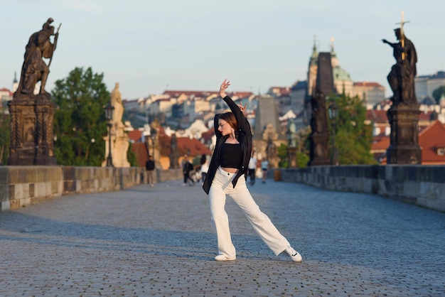 アクティブなプラハの旧市街の石橋で踊るカジュアルでスタイリッシュな服を着た若い女性