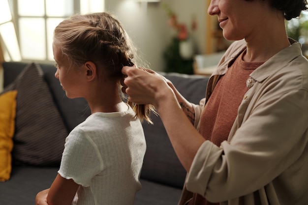 Young woman in casualwear plaiting braids on head of her cute daughter