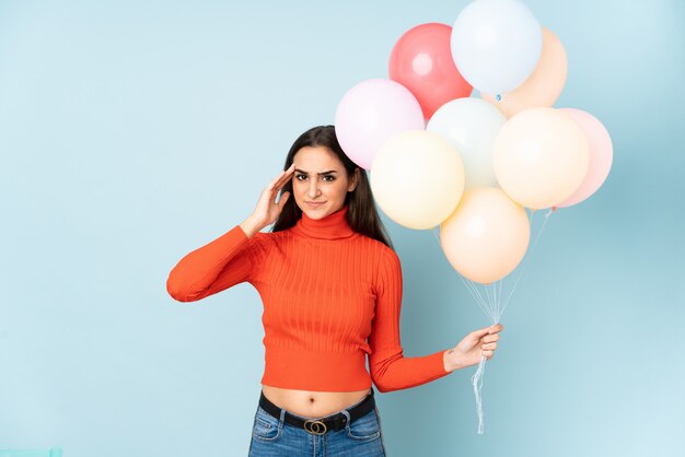 Young woman catching many balloons on blue wall unhappy and frustrated with something.