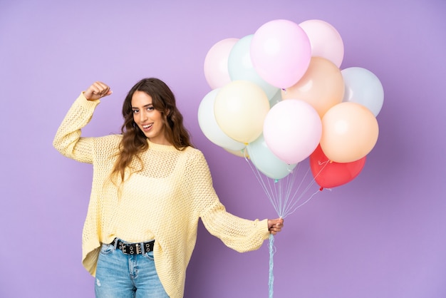 Young woman catching many balloons over on purple wall celebrating a victory