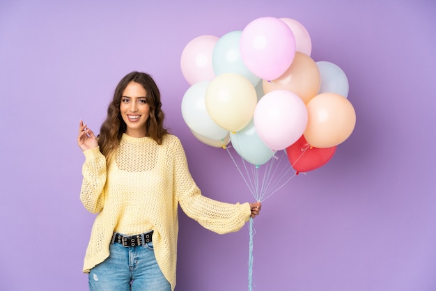 Young woman catching many balloons over on purple wall laughing