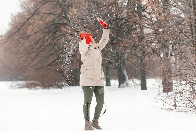 Young woman catching snowflakes in the air in winter park