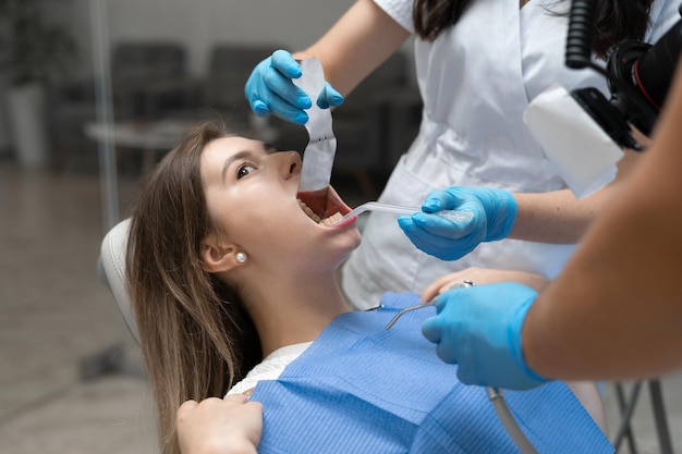 백인 인종의 젊은 여성이 입을 벌리고 있는 치과의사에 앉아 있다. 간호사와 교정의사의 손이 환자의 입을 조작합니다. 공간을 복사합니다.