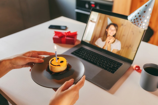 Giovane donna che celebra il suo compleanno a casa con gli amici in videochiamata