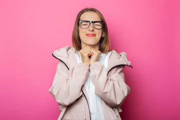 Young woman celebrating in pink jacket, pink isolated background.