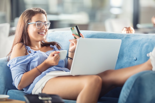 Молодая женщина в кафе с кредитной картой и ноутбуком удобно покупает их через Интернет