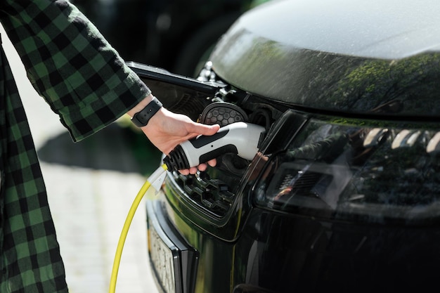 Young woman charging an electric car by plugging the cable in charging station