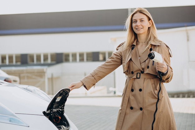 Young woman charging her electric car with charging pistol