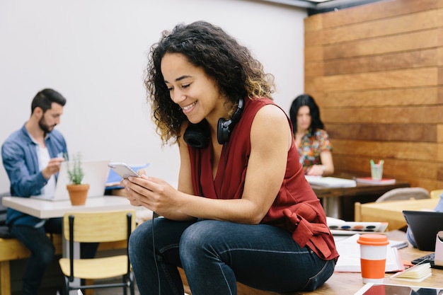 Giovane donna che chiacchiera con il suo smartphone nell'espace di coworking